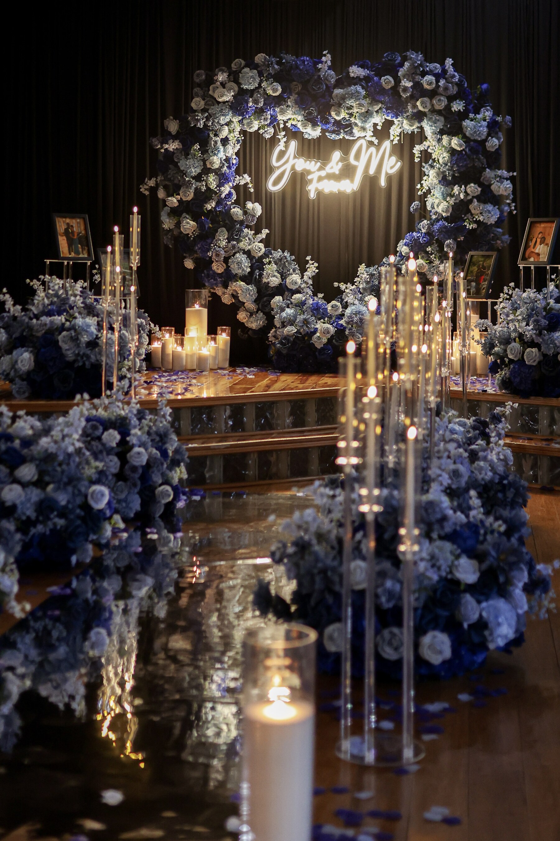 Royal blue and white heart floral arch with You and Me Forever neon sign, candlelit aisle